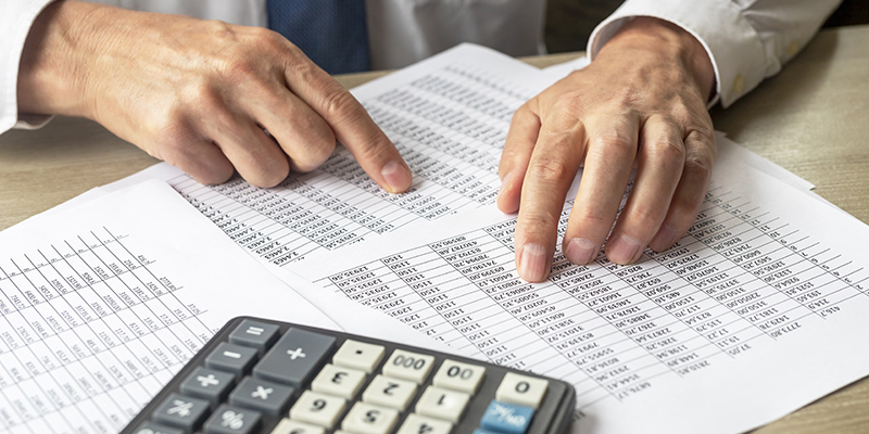 Businessman Analyzing Accounting financial Documents With Calculator on foreground At Desk In Office